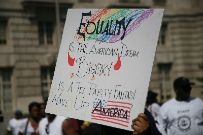 In case you can't read the sign, it says: "EQUALITY IS THE AMERICAN DREAM. BIGOTRY (with parenthetical red Devil's horns) IS A TEA PARTY FANTASY. WAKE UP AMERICA."